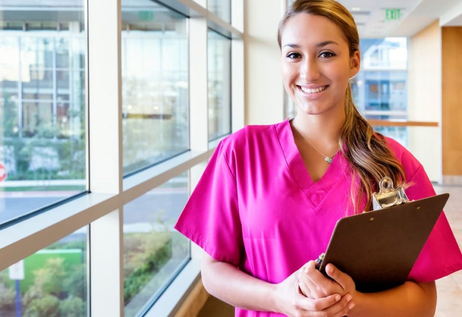 healthcare worker in pink scrubs holding a clipboard.